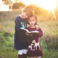 Two children standing in grass reading a book