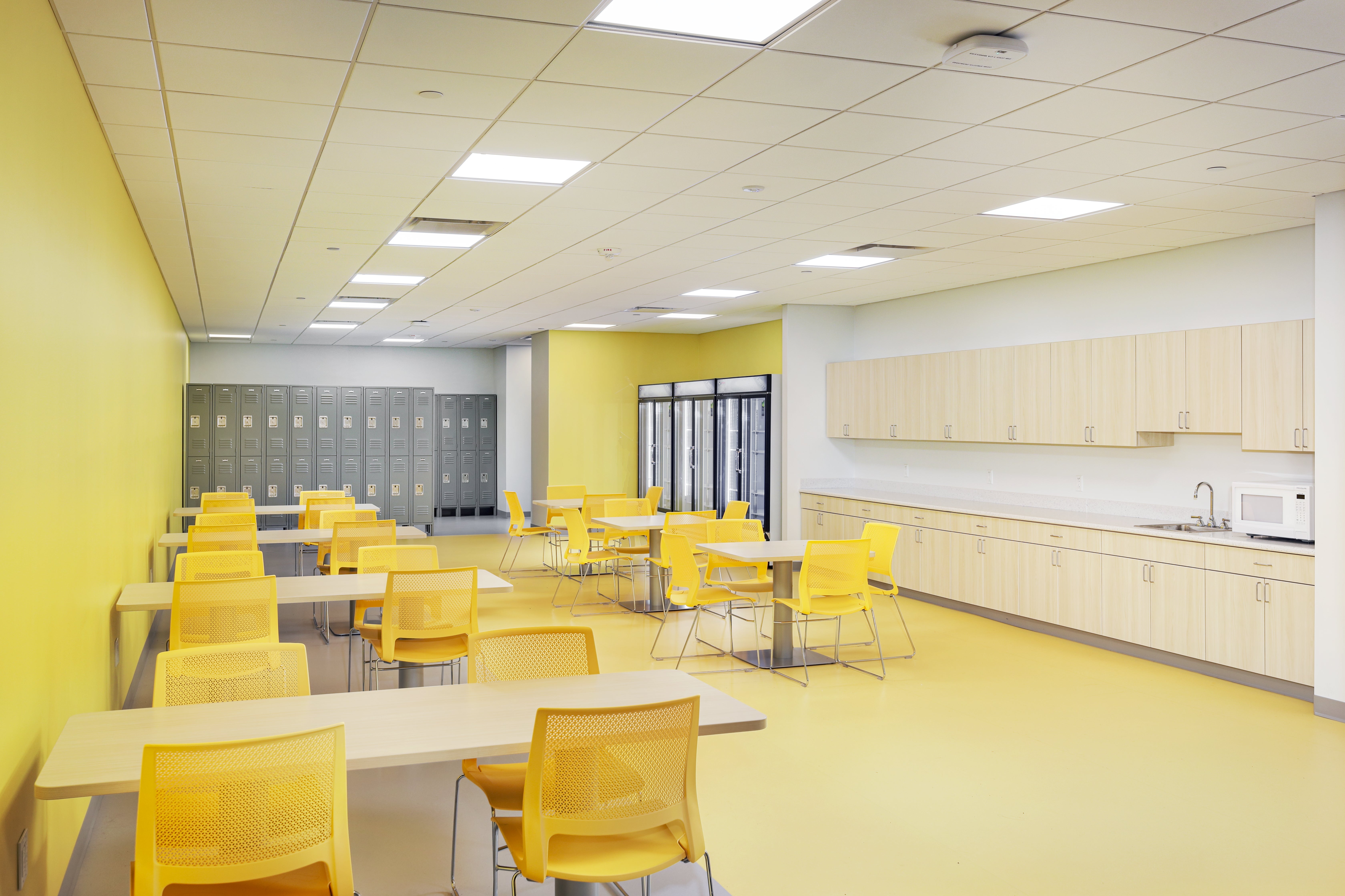 Room with lockers and with yellow accents, tables and chairs