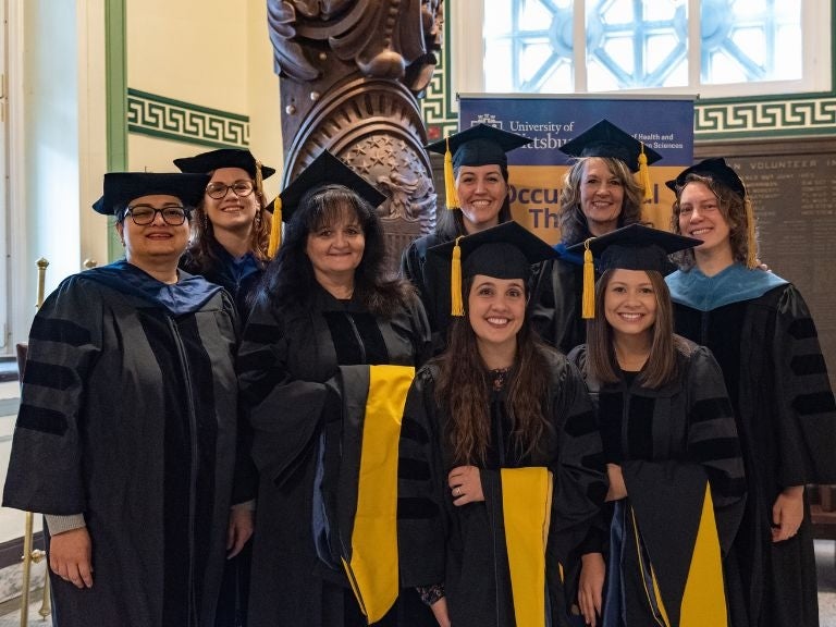 6 doctoral graduates in cap and gown attire with professor and department chair
