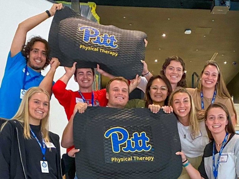 students holding up floor mats that say Pitt Physical Therapy