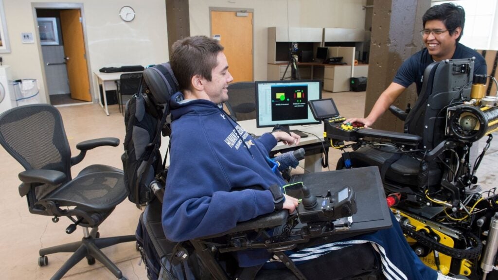Man sitting in an electric wheelchair interacting with a technician.