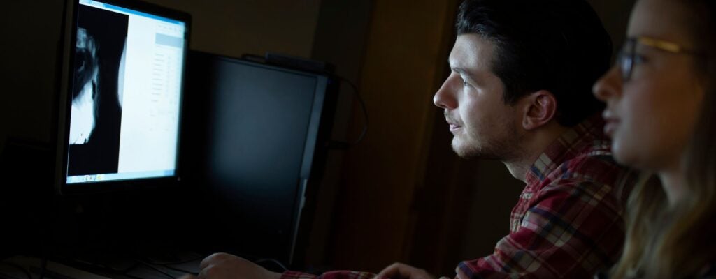 Two students looking at a screen in a dark room observing imaging of inside of an ear canal.