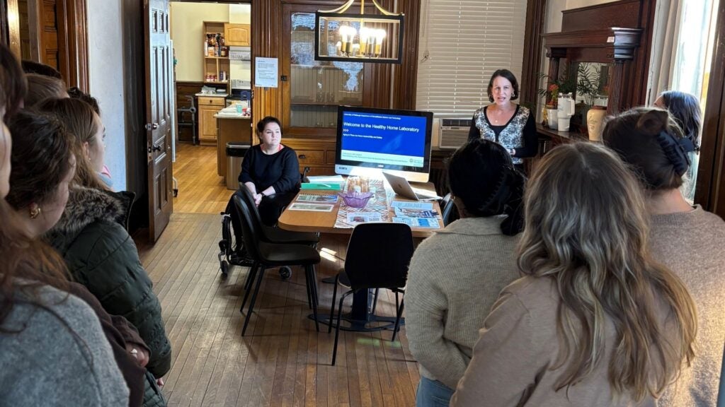 Group listening to a lecture in a dining room space fitted with a monitor.