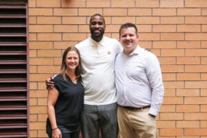 Three people posing for a group photo in front of an orange-brick wall.