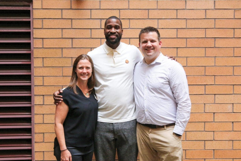 Three people posing for a group photo in front of an orange-brick wall.