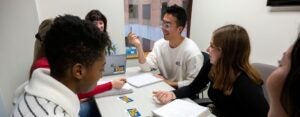 Male and female students sitting around a small table collaborating on work.