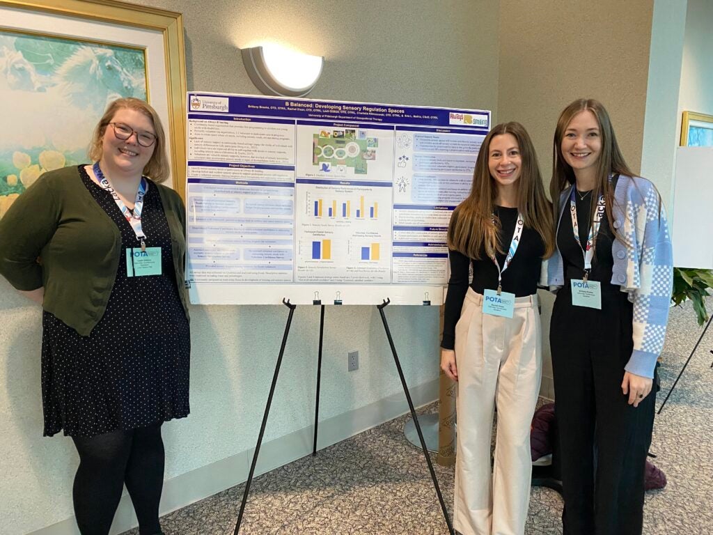 Three students standing next to a research poster