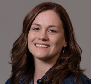 Woman with curled auburn hair wearing a dark denim blouse and a silver earring.