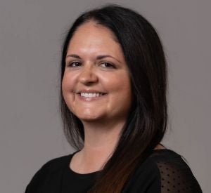 Woman with dark straight hair wearing a black blouse with a mesh pattern on the side with black polka dots.