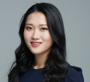 Woan with very dark hair curled at the bottom wearing a navy blue blouse.