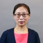 Woman with black hair pulled back wearing a navy blue sweater over a pink blouse.