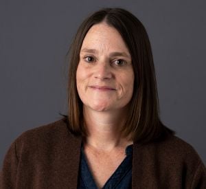 Woman with dark short hair wearing a brown sweater over a black blouse.