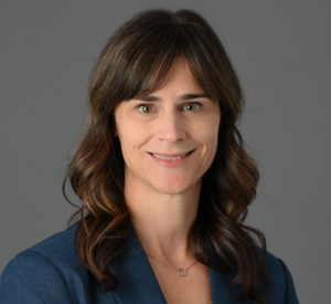 A portrait photo of a woman with long brown hair and short banks wearing a blue dress jacket.