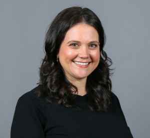 Woman with dark brown curly hair wearing a black sweater.