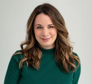 A woman with curled brown hair with blonde highlights wearing a dark green sweater.