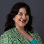 Woman with short dark hair wearing a bright green blazer with light blue, pink and yellow stitching over a teal shirt.