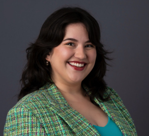 Woman with short dark hair wearing a bright green blazer with light blue, pink and yellow stitching over a teal shirt.