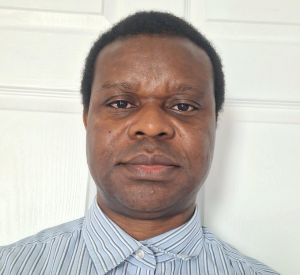 Man with dark short hair wearing a light blue colored shirt with white and gray stripes.