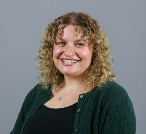 Woman with blonde curly hair wearing a green cardigan over a black shirt with a silver necklace.