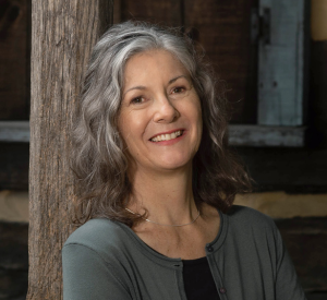 Woman with dark brown and gray hair wearing a gray sweater over a black shirt.