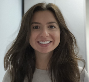A woman with long brown hair wearing a tan sweater.
