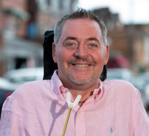 A man with short dark and gray hair and goatee wearing a light pink collared shirt