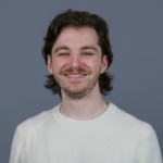 Man with short brown hair wearing a white sweater.