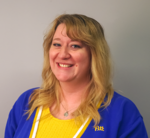 Woman with blonde hair wearing a royal blue and yellow Pitt cardigan over a yellow knit sweater.