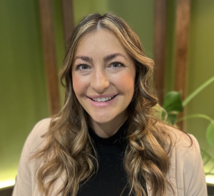 Woman with dark blonde curled hair wearing a white cardigan over a black shirt.