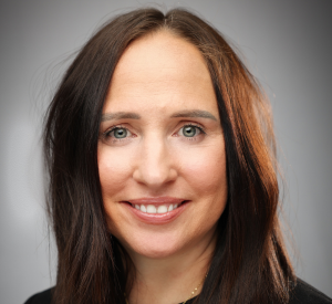 Woman with dark auburn hair wearing a black shirt and a gold necklace.