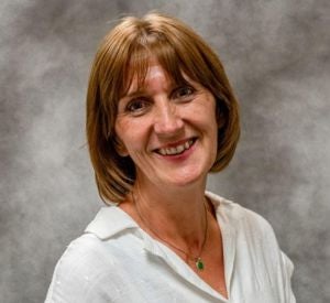 Woman with short auburn hair and bangs wearing a white collared blouse.