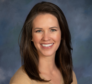 Woman with dark brown hair wearing a tan shirt and pearl earrings.