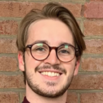 Man with brown hair and glasses wearing a dark red shirt.