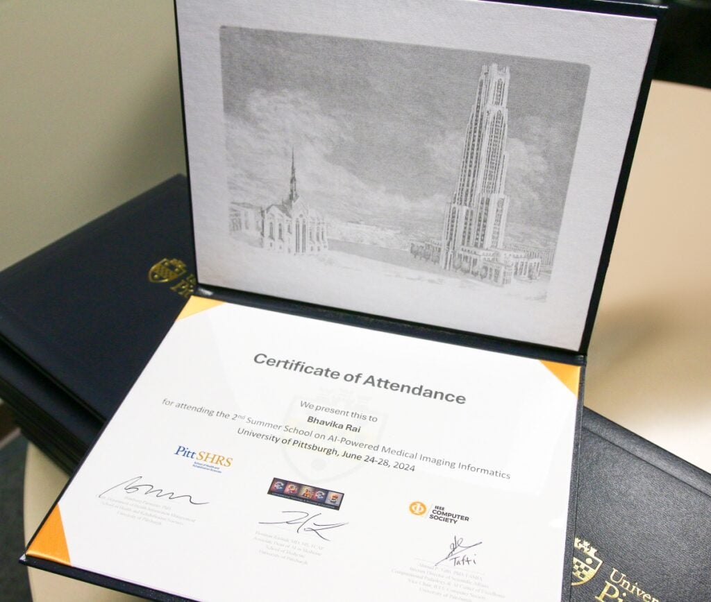 A portfolio is opened to show a signed certificate with an artist rendering of the Cathedral of Learning.