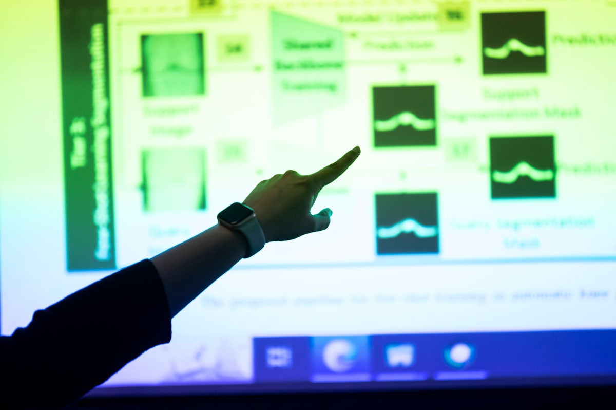 An arm and finger point to a projected screen showing blurred images of data