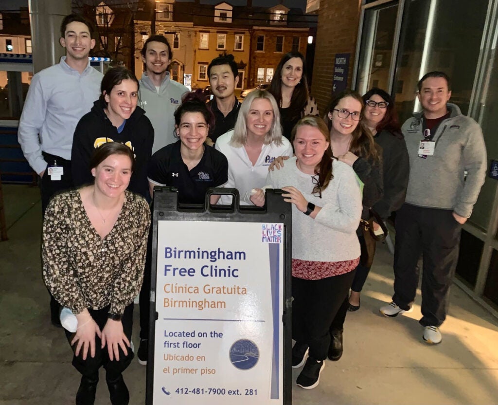 A group of people pose for a night photo in front of a sign for Birmingham Free Clinic