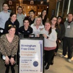 A group of people pose for a night photo in front of a sign for Birmingham Free Clinic