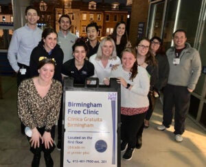 A group of people pose for a night photo in front of a sign for Birmingham Free Clinic