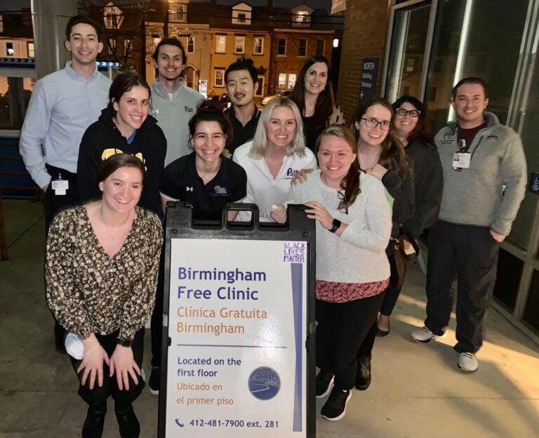 A group of people pose for a night photo in front of a sign for Birmingham Free Clinic