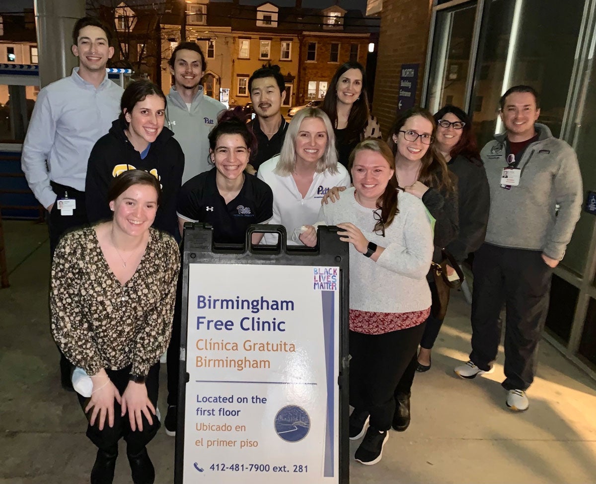 A group of people pose for a night photo in front of a sign for Birmingham Free Clinic
