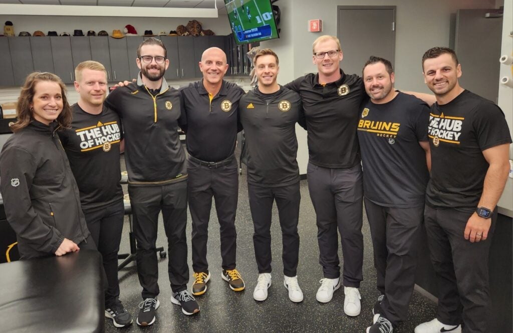 A group of seven men and one woman wearing black workout clothes pose for a photo