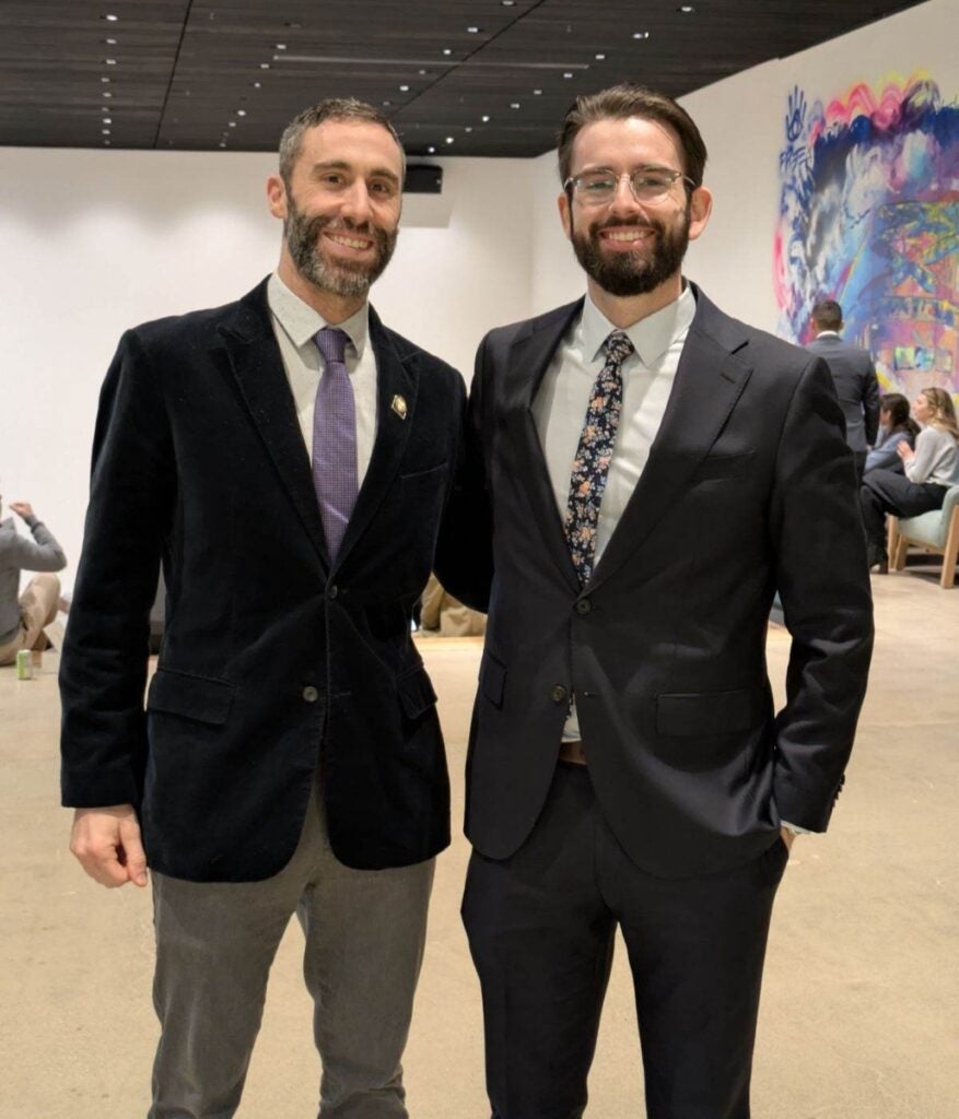 Two men with beards wearing suit jackets and ties pose for a photo