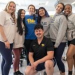 A group of seven students wearing Pitt t-shirts and sweatshirts pose for a photo