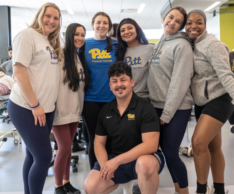 A group of seven students wearing Pitt t-shirts and sweatshirts pose for a photo