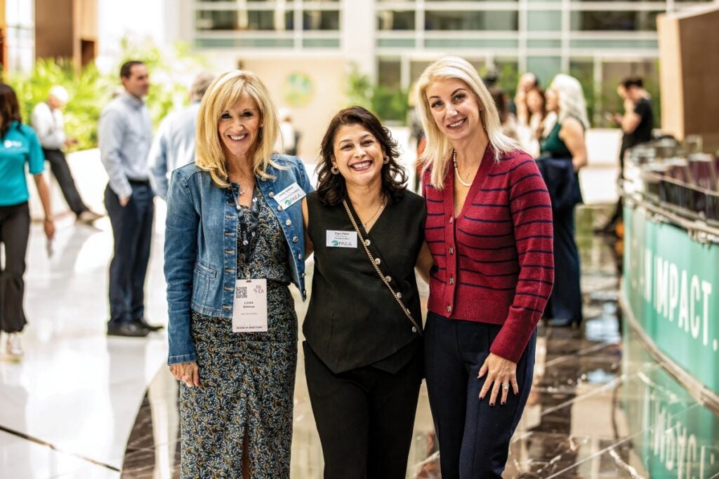 Three women at a conference smile and pose together