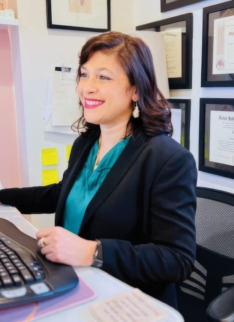 A woman with medium length brown hair wearing a dark blue jacket sits at a computer