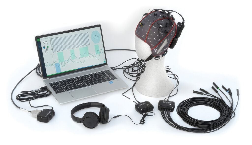 A display of electronics shows a computer laptop, headphones, a head cap of electronic sensors and different cables
