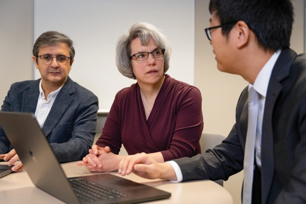 Two men and a woman sit in front of a laptop computer having a discussion