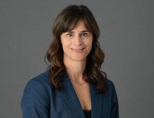 A portrait photo of a woman with long brown hair and short banks wearing a blue dress jacket
