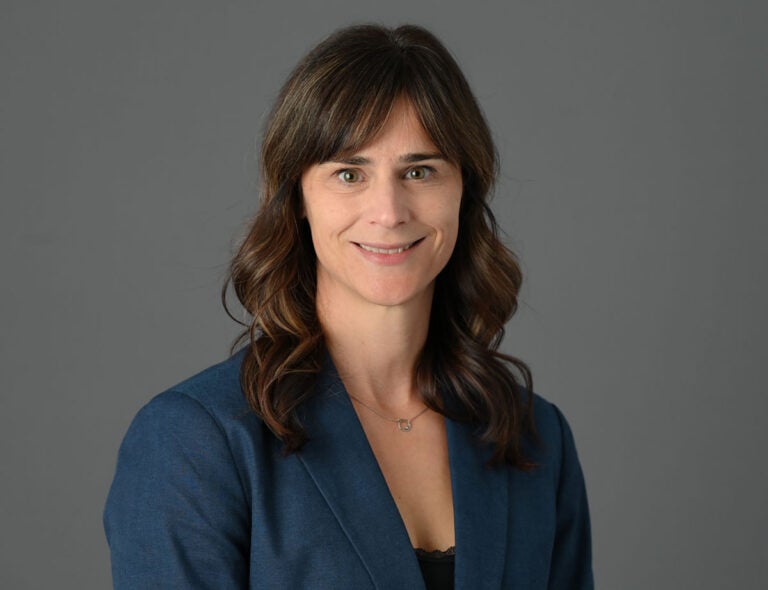 A portrait photo of a woman with long brown hair and short banks wearing a blue dress jacket